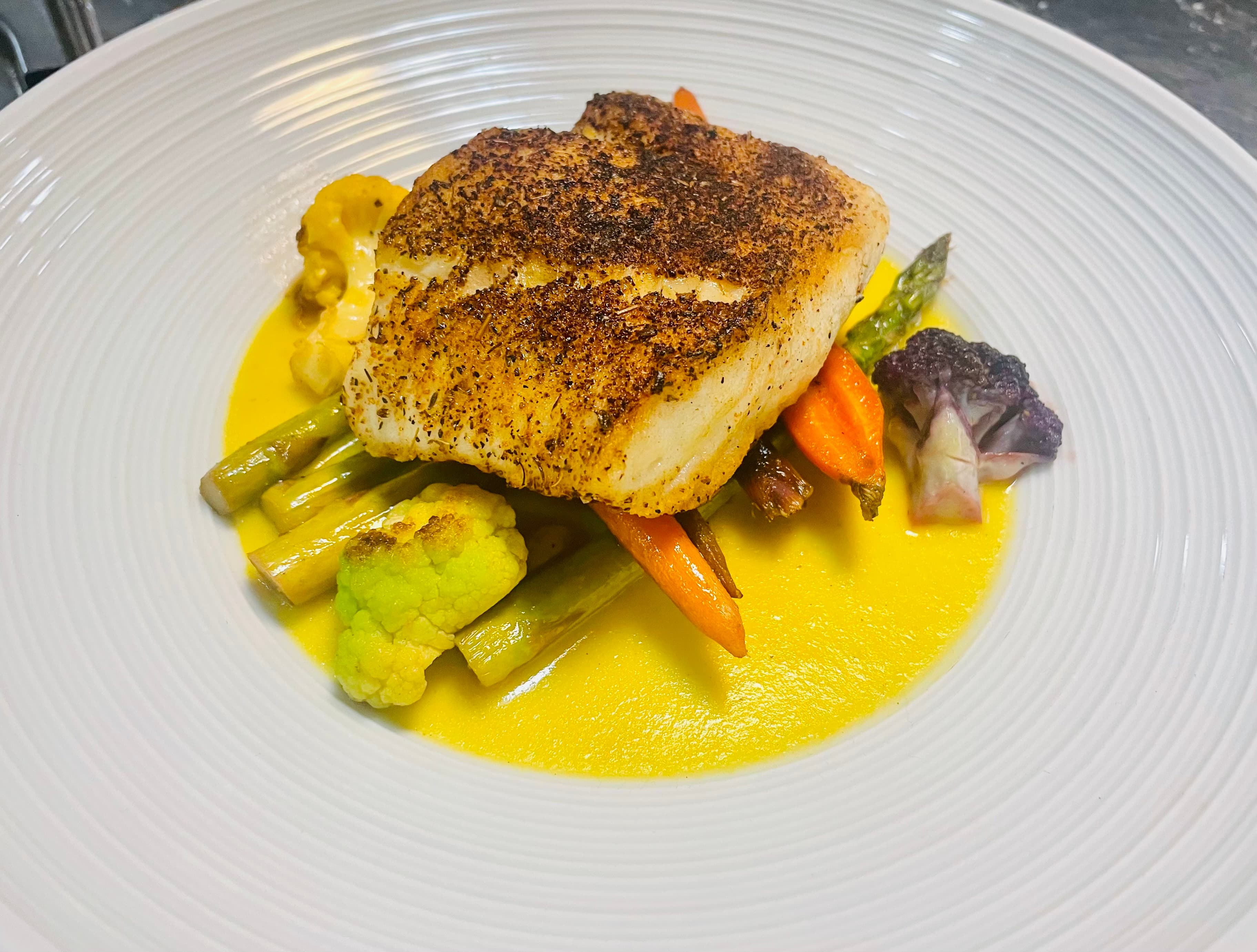 Seared spiced fish over roasted vegetables in a golden sauce